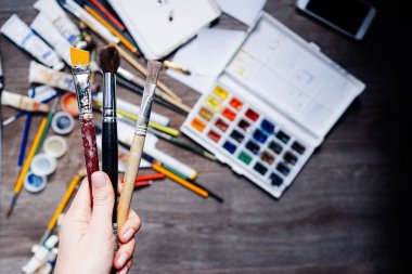 bir ahşap zemin üzerinde bir sürü sanatsal malzemeleri, boya, kalem, fırça tutan bir kadın yalan.