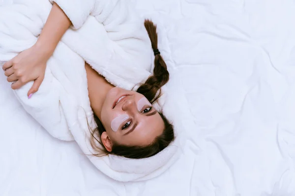 Feliz chica sonriente se encuentra en una cama en un vestido de terciopelo blanco — Foto de Stock