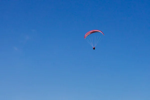 En röd fallskärm flyger över den blå himlen — Stockfoto