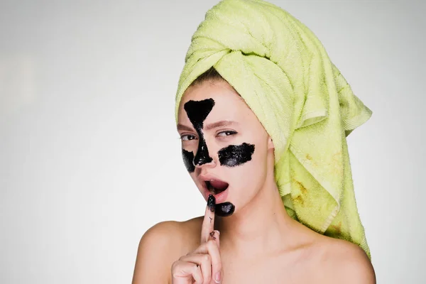 Ładna, młoda dziewczyna z zielony ręcznik na głowie ma wyrażać czarna maska na obszarach problemowych na jej twarzy — Zdjęcie stockowe