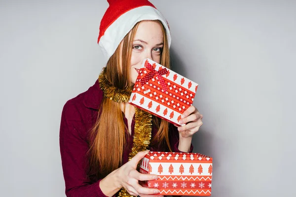 Glückliche rothaarige Mädchen erhielt ein Geschenk für das neue Jahr, auf ihrem Kopf eine rote Kappe wie Weihnachtsmann claus — Stockfoto