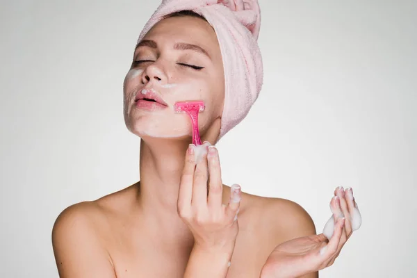 Aranyos lány a fején rózsaszín törülközővel shaves arcát, mint egy ember — Stock Fotó