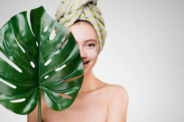 Atractiva linda chica con una toalla en la cabeza sostiene una hoja verde, disfrutando de tratamientos de spa — Foto de Stock