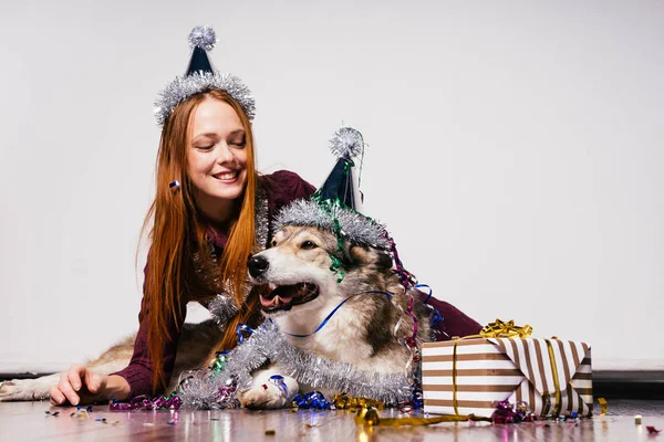 Heureuse fille aux cheveux roux avec un chapeau sur la tête s'assoit sur le sol avec son chien célébrant la nouvelle année 2018 — Photo