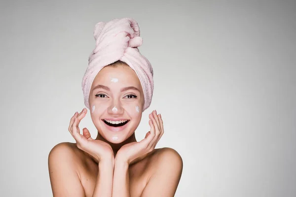 Heureuse fille souriante avec serviette rose met sur le visage crème blanche hydratante — Photo