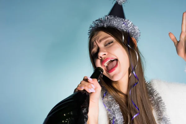 Смешная пьяная девушка празднует Новый год, поет в бутылке шампанского — стоковое фото