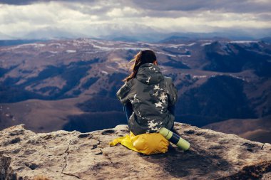 Sarı bir sırt çantası ile genç kız dağ doğanın keyfini bir uçurumun kenarında oturur