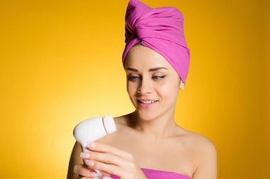 sevimli genç kız başında pembe havlu ile onun yüz temizliği için elektrikli bir fırça tutar