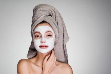 Kafasındaki bir havlu ile çekici bir genç kız beyaz bir besleyici maske yüzüne karşı uygulanan.