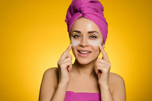 cute young girl with a pink towel on her head glues patches under the eyes