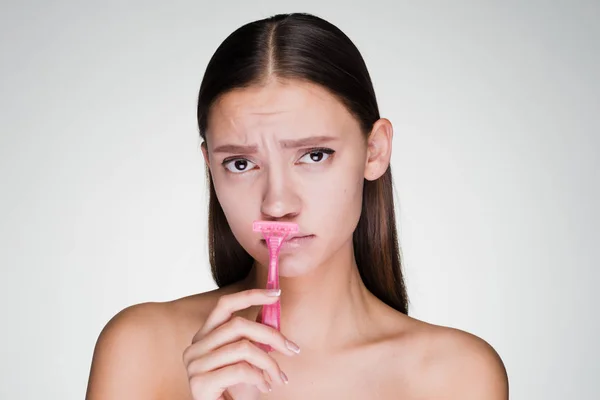 Грустная молодая девушка бреет усы розовой бритвой — стоковое фото