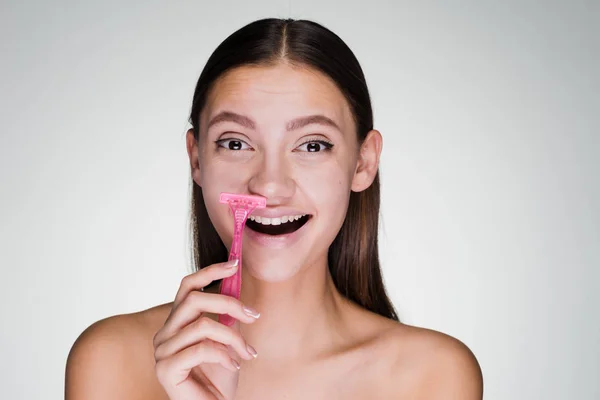 Смеющаяся молодая девушка бреет усы розовой бритвой — стоковое фото