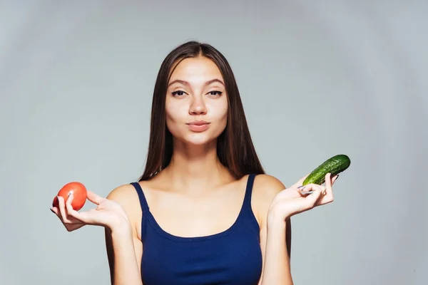 Jistý mladá dívka v modré košili se chce zhubnout, drží okurky a rajčat — Stock fotografie