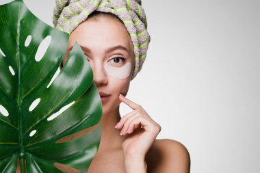 sevimli genç kız başında, bir havlu ile tutan bir yaprak yeşil gözleri yamalar altında bir spa sahiptir