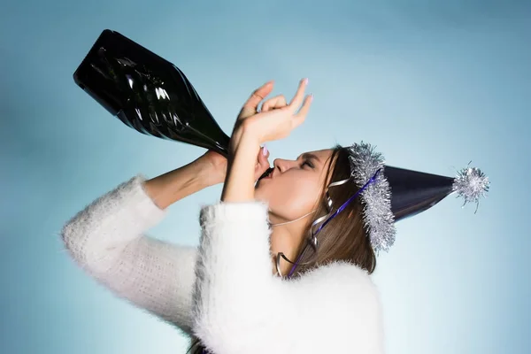 Смешная молодая девушка в кепке празднует Новый 2018 год, пьет шампанское из бутылки — стоковое фото