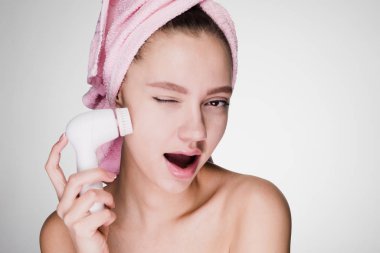 genç kız başında pembe havlu ile elektrikli bir fırça yardımıyla yüz cildin derin bir temizlik yapar