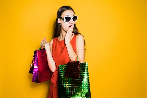 Удивленная молодая девушка-шопоголик в солнцезащитных очках купила много подарков на новый год, удивленная скидками — стоковое фото