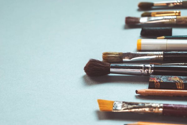 на синем столе много художественных кистей и карандашей
