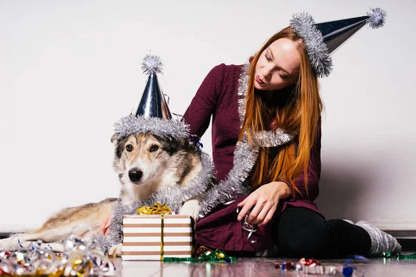 Рыжая молодая девушка в праздничной кепке сидит на полу со своей большой собакой в ожидании нового года — стоковое фото