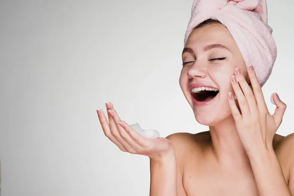 Счастливая смеющаяся девушка с полотенцем на голове, нанося пену для очищения лица — стоковое фото
