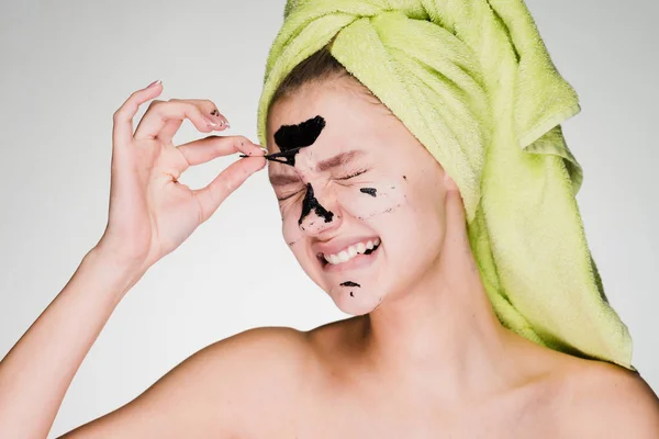 Грустная молодая девушка с зеленым полотенцем на голове снимает черную маску с лица — стоковое фото