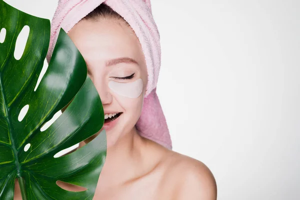 Zaskoczony szczęśliwy dziewczyna z ręcznikiem na głowie, przytrzymując zielony liść, pod oczy patche, day spa — Zdjęcie stockowe