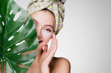 gözleri yamalar altında bir spa zevk sevimli gülümseyen kız yaprak yeşil holding başında bir havlu ile