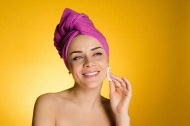 genç kız başında pembe havlu ile gülümseyen bir pamuk ile cildi temizler