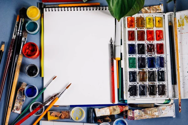 Em uma mesa azul são suprimentos artísticos, papel branco e cores coloridas — Fotografia de Stock