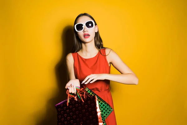 Stylish young girl shopaholic in sunglasses bought a lot of gifts for the new year — Stock Photo, Image