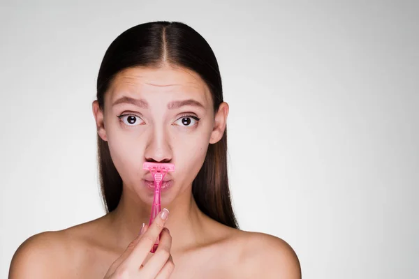 Милая грустная девушка бреет усы розовой бритвой — стоковое фото