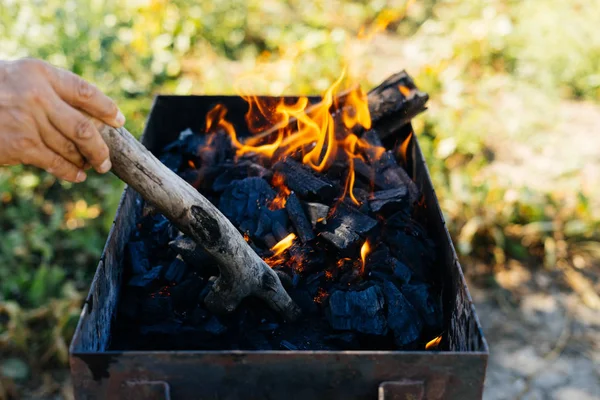 Em um piquenique na natureza um homem acende um fogo em um churrasco — Fotografia de Stock