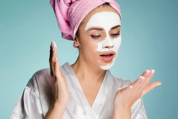 Menina bonito com uma toalha rosa na cabeça, aplicando uma máscara hidratante branco em seu rosto — Fotografia de Stock