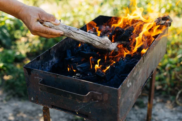 Na natureza em um piquenique um homem acende um fogo em um churrasco — Fotografia de Stock