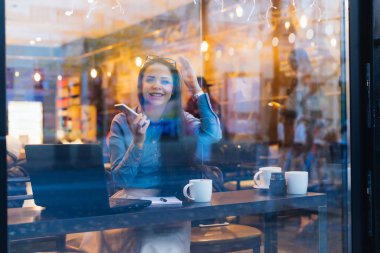 mutlu gülümseyen kız mavi gömlekli bir kafede oturan ve telefonda konuşurken