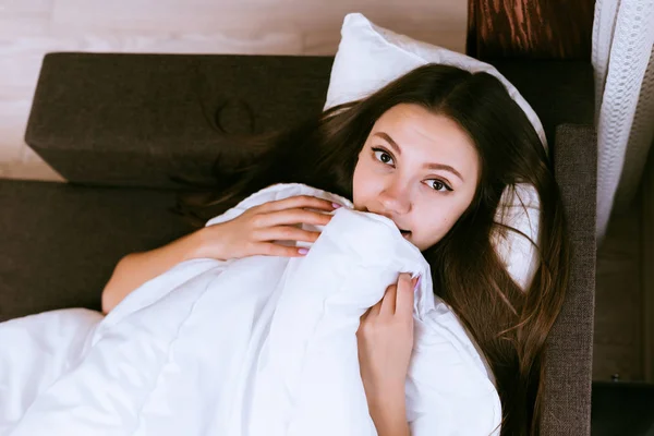 Niedliche junge Mädchen liegt im Bett unter einer weißen Decke, will nicht aufstehen — Stockfoto