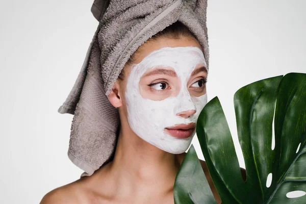 Krásná mladá dívka s ručníkem na hlavě použita bílá výživnou maskou na tváři — Stock fotografie