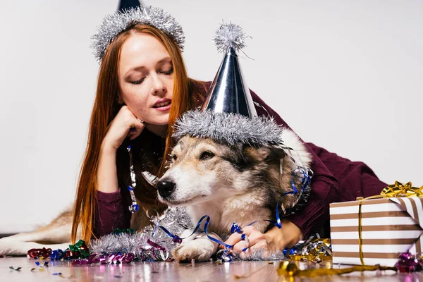 Belle fille aux cheveux roux dans un chapeau de fête s'assoit sur le sol avec son chien, attendant la nouvelle année — Photo