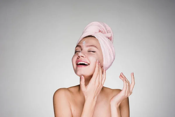 Feliz chica sonriente con toalla rosa en la cabeza aplicando crema hidratante blanca en la cara — Foto de Stock