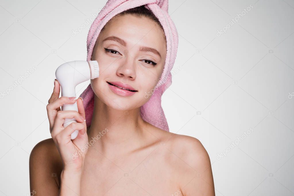 cute young girl with a pink towel on her head doing a deep cleansing of the skin of the face with an electric brush