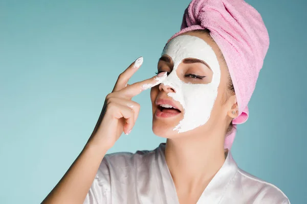 Attractive young girl with a pink towel on her head puts a white nutritious mask on her face — Stock Photo, Image