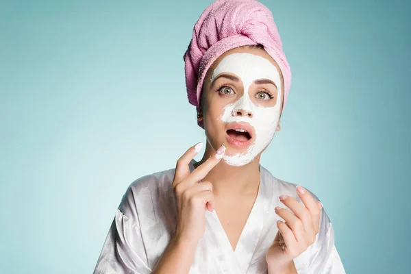 Αστείο κορίτσι με μια ροζ πετσέτα στο κεφάλι της βάζει ένα λευκό ενυδατική μάσκα στο πρόσωπό της — Φωτογραφία Αρχείου