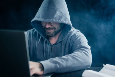 erkek hacker'bir kazak bir kukuleta ile bir dizüstü bilgisayar oturuyor