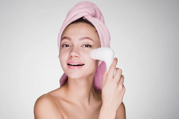 Женщина с полотенцем на голове очищает лицо щеткой для глубокой очистки — стоковое фото