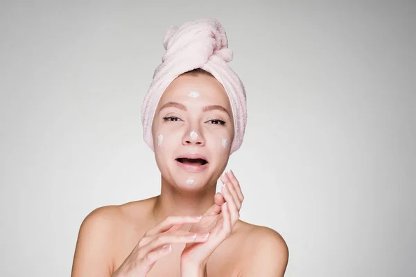 Mulher com uma toalha na cabeça aplicada creme no rosto — Fotografia de Stock