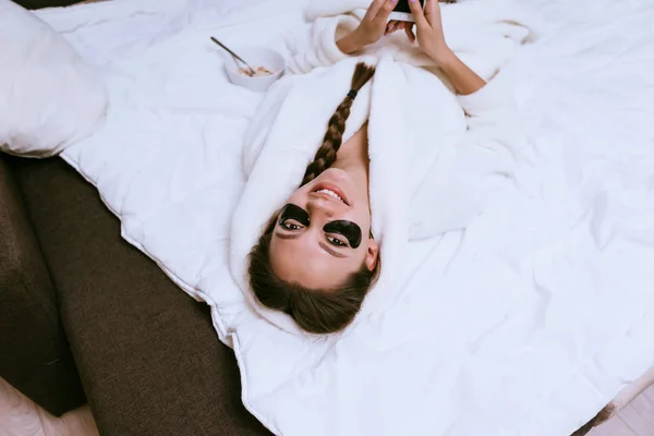 Lycklig kvinna sätta fläckar under ögonen och lögner på sängen — Stockfoto