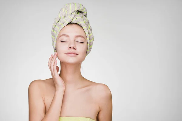 Vrouw met een handdoek op haar hoofd sloot haar ogen tegen een grijze achtergrond — Stockfoto