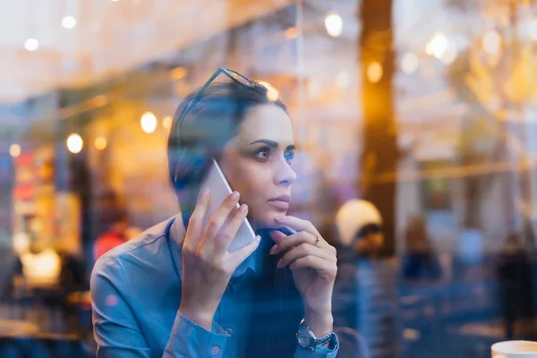 Женщина сидит за окном и разговаривает по телефону — стоковое фото