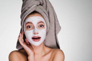 Kafasındaki bir havlu ile mutlu kadın beyaz bir maske yüzünde temizlik uygulanan