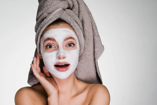Mulher feliz com uma toalha na cabeça aplicou uma máscara de limpeza branca em seu rosto — Fotografia de Stock